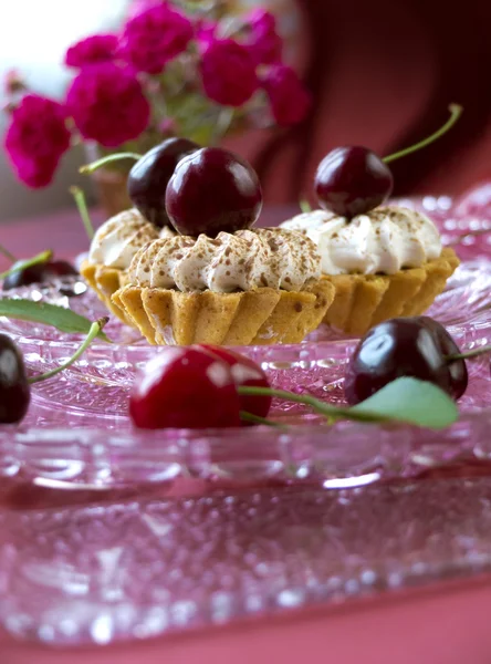 Торты (кексы) с темными вишнями на стеклянной тарелке — стоковое фото