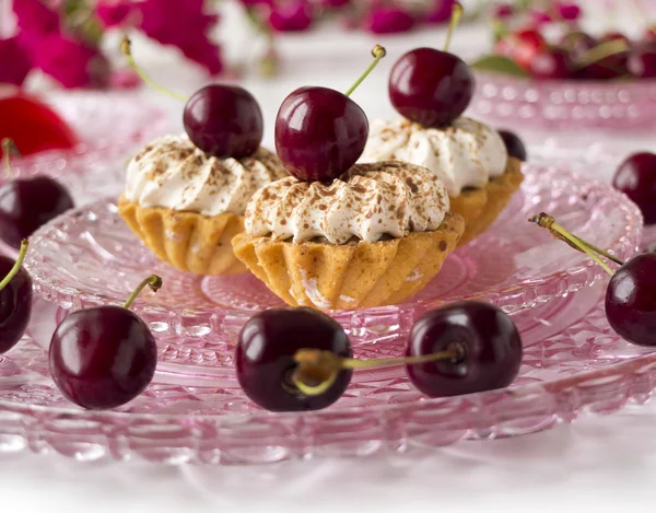 Pasteles con cerezas, crema batida y flores — Foto de Stock