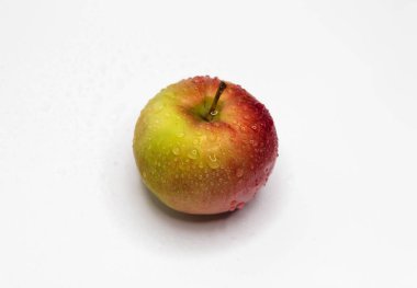 Derisinde su damlaları olan küçük bir elma beyaz bir zeminde yatıyor.