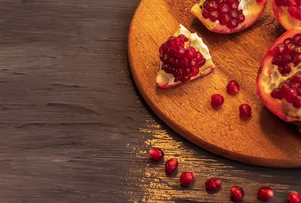 Düz olmayan parçalara ayrılmış sulu nar yuvarlak bir tahtanın üzerinde yatıyor.