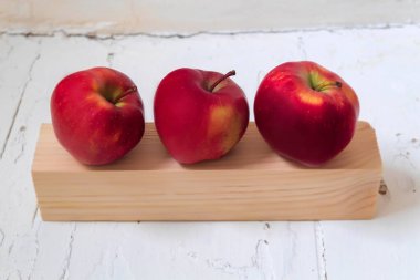 Resim taze ve çiğ gıdanın bir resmini gösteriyor. Bunlar elma. Kırmızı renkteler. Elmalar ahşap bir tahtaya ve onun yanına yerleştirilir.