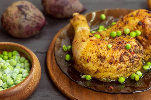 The photo shows a picture of fine food. This is chicken meat in spices, baked in the oven at home. The chicken is on the plate. The plate stands on a wooden stand. All the items are laid out on a wooden table. Green peas on chicken meat. In the backg