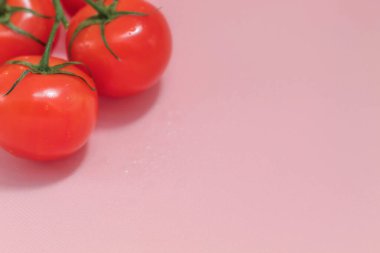 Pembe arka planda, taze olgun gıdanın görüntüsü var. Bunlar sebze. Yeşil dalda kırmızı domatesler. Hepsi bir bütün ve derilerinde.