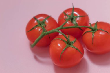 Pembe arka planda, taze olgun gıdanın görüntüsü var. Bunlar sebze. Yeşil dalda kırmızı domatesler. Hepsi bir bütün ve derilerinde.