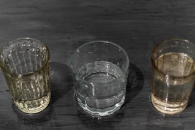 The photo shows the image of glasses with water. There is a lot of water around. The glasses stand on a dark gray background