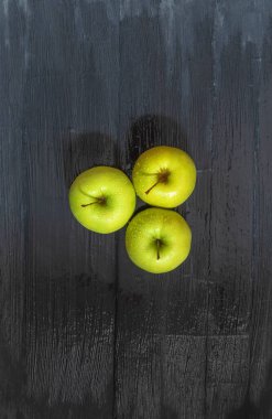Fotoğraf taze meyve görüntüsünü gösteriyor. Bunlar elma. Merkezde, siyah bir tahta masanın üzerinde yatıyorlar.