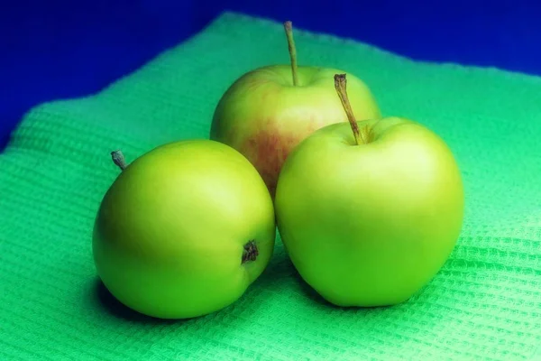 The photo shows an image of green fresh apples in the amount of three pieces of almost the same size. Apples are ripe, whole and useful for the human body