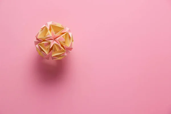 Multicolor handmade modular origami ball or Kusudama Isolated on pink background. Visual art, geometry, art of paper folding, paper crafts. Top view, close up, selective focus, copy space.