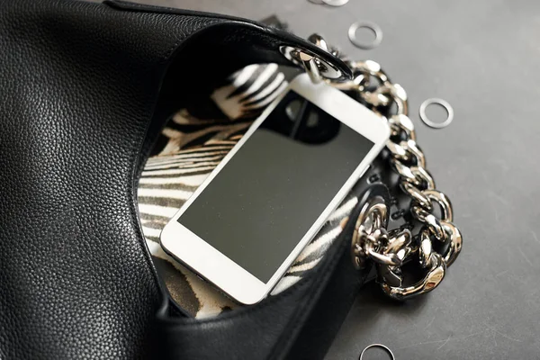 Black leather bag with chain, white phone, zebra print, silver thin rings on a black background