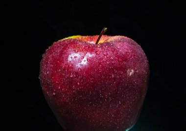 Siyah arkaplanda su damlacıklarıyla kaplı koyu kırmızı elma.