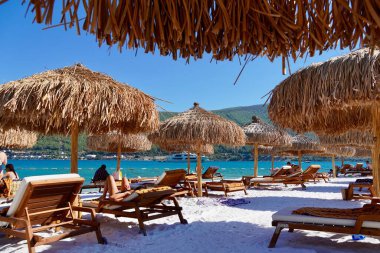 Bodrum, Türkiye - Ağustos 2020: Ege Denizi 'nin zümrüt suyuyla Lux Hotel' in kar beyazı plajı. Yatlar. İnsanlar plajda güneşleniyor. Kumsalda güneşli yataklar. Rahatlatıcı Lüks Eğlence Konsepti