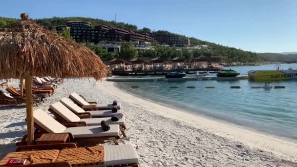 4 Kエメラルドラグーンは、トルコのLujo Luxury Hotelの白いビーチにある雪の白いエコヨット、サンラウンジャー、竹の傘で常緑の丘を見下ろす。 — ストック動画