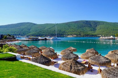 Bodrum, Türkiye - Ağustos 2020 Lux Hotel 'in kar beyazı plajı Ege Denizi' nin zümrüt suyuyla. Yatlar. İnsanlar kumsalda güneşleniyor. Kumsalda güneşli yataklar. Lüks Gebelik Rahatlatıcı. Cennet