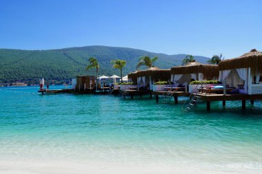 Bodrum, Türkiye - Ağustos 2020 Lux Hotel 'in kar beyazı plajı Ege Denizi' nin zümrüt suyuyla. Yatlar. İnsanlar kumsalda güneşleniyor. Kumsalda güneşli yataklar. Lüks Gebelik Rahatlatıcı. Cennet