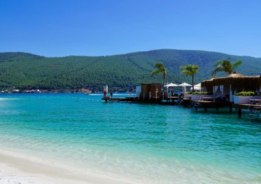 Bodrum, Türkiye - Ağustos 2020 Lux Hotel 'in kar beyazı plajı Ege Denizi' nin zümrüt suyuyla. Yatlar. İnsanlar kumsalda güneşleniyor. Kumsalda güneşli yataklar. Lüks Gebelik Rahatlatıcı. Cennet