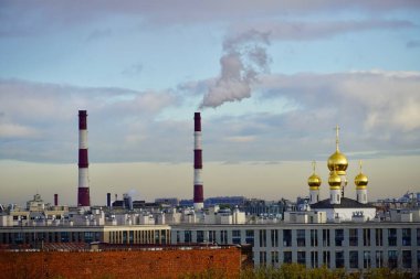 Endüstriyel şehir manzarası, dumanı tüten boruları ve arka planda bulutlu bir gökyüzü olan çelik fabrikası. Şehir manzarası kontrastı - bitki boruları ve kilisenin kubbeleri güzel bir gökyüzüne karşı.