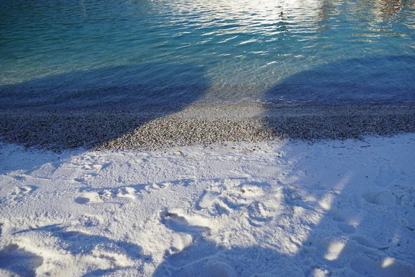 Snow white sand and pebbles on the ocean coast near the emerald ocean at sunset — Stock Photo, Image