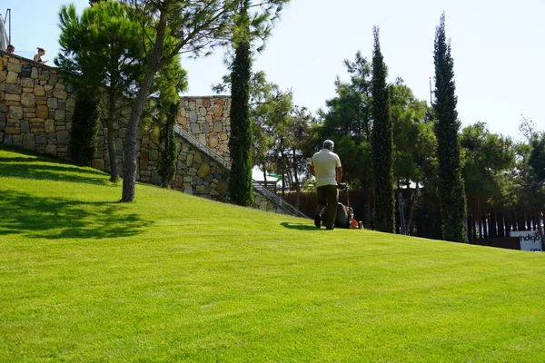 Бодрум, Туреччина - серпень 2020 дорослий чоловік у капелюсі і масці зрізає газон в спекотний день влітку. Працюйте в будинку та саду, дбайте про територію. Служба в готелі. — стокове фото