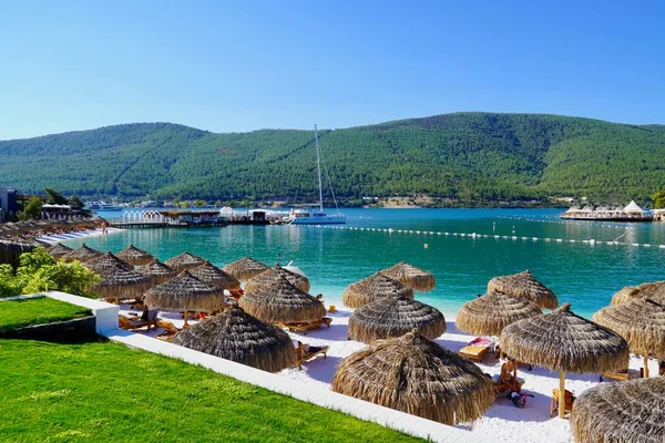 Bodrum, Türkiye - Ağustos 2020 Unutulmaz deniz tatilleri için uygun plajları ve kıyıları olan Ege Denizi 'nden bir inci. Tatil afişi. Hotel Lux Lujo plajı, gün doğumunda. Bambu şemsiyeler, gök mavisi okyanus.