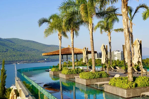 Bodrum, Türkiye - Türkiye 'nin güzel manzarası 2020 Ağustos' ta ön planda boş yüzme havuzu ile lüks bir tatil köyü. Yeşil tepeler, palmiyeler ve gök mavisi okyanuslar. Panoramik görünüm