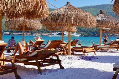 Bodrum, Türkiye - Ağustos 2020 Unutulmaz deniz tatilleri için uygun plajları ve kıyıları olan Ege Denizi 'nden bir inci. Tatil afişi. Hotel Lux Lujo plajı, gün doğumunda. Bambu şemsiyeler, gök mavisi okyanus.