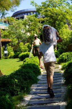 Bodrum, Türkiye - Ağustos 2020 Şapkalı Yetişkin Adam elinde hortumla bahçesini suluyor. Evde ve bahçede çalış, toprakla ilgilen. Oteldeki servis elemanları. 