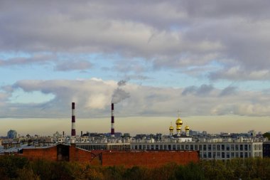 Endüstriyel şehir manzarası, dumanı tüten boruları ve arka planda bulutlu bir gökyüzü olan bir çelik fabrikası. Kentsel manzara kontrastı - bitki boruları ve kilisenin kubbeleri güzel bir gökyüzüne karşı.