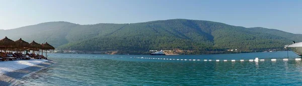 Bodrum, Törökország - augusztus, 2020 Lenyűgöző panoráma a szigetre pálmafákkal, fehér homokkal, türkizkék óceáni vízzel és kék égbolttal, Vízi bungaló, fehér hajók — Stock Fotó
