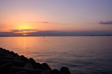 Serene sunset over calm ocean with silhouetted breakwater.