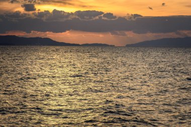 Golden sunset over choppy sea with distant hills
