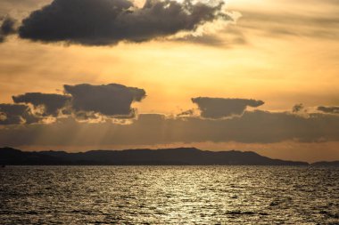Golden sunset over the ocean with silhouetted clouds and distant hills.