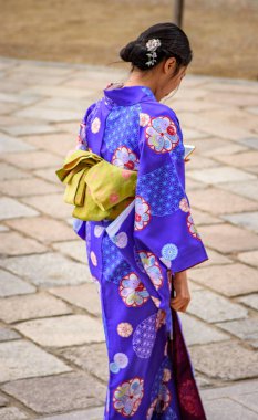 Geleneksel kimonolu bir kadın çiçek desenli, elinde telefon, 10 Aralık 2017 'de Japonya' nın Kyoto şehrinde taş kaldırımda yürüyor.