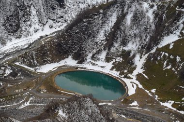 Karlı dağlarla çevrili dairesel bir turkuaz göl manzarası..