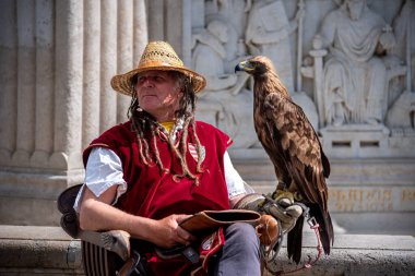 30 Nisan 2023 'te Macaristan' ın Budapeşte kentinde, kolunda altın kartal olan hasır şapkalı ve kırmızı yelekli bir Şahin oturuyordu.