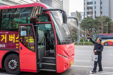 19 Kasım 2023 'te Güney Kore, Seul' de bir şehir caddesinde kırmızı bir tur otobüsünü hortumla temizleyen bir işçi.