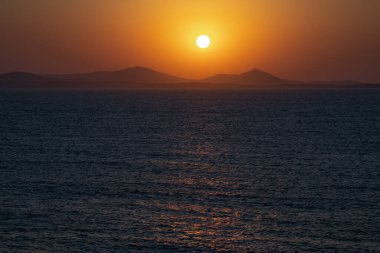 Sakin bir denizin üzerinde gün batımı Uzak dağların silueti.