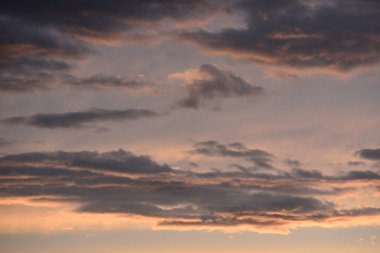 Gün batımında dağınık bulutlarla, yumuşak pembe ve turuncu renkler içeren sakin bir gökyüzü..