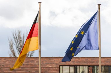 Almanya ve Avrupa Birliği 'nin bayrakları bulutlu bir gökyüzüne karşı rüzgarda sallanıyor