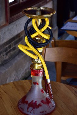 Renkli bir hortumla dekoratif bir nargile, ahşap bir masanın üzerine yerleştirilmiş, tabanında bir deve tasarımı var.