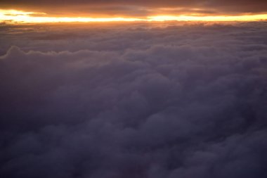 Arka planda günbatımı olan bulutların hava görüntüsü turuncudan mora doğru bir renk eğimini gösteriyor.