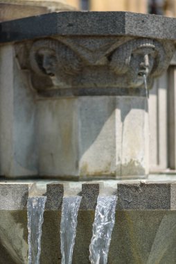 Fıskiyelerden akan suyla dolu taştan bir çeşmenin yakınında..