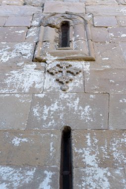 Eski bir kilise binasında çapraz ve dar pencereli antik taş duvar.