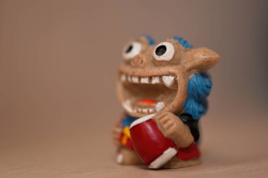 Kırmızı bir davul tutan, abartılı özelliklere sahip, kaprisli bir kil heykelciğin yakın çekimi.