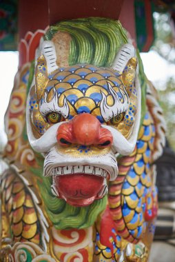 Renkli boyalı ejderha koruyucu başı süslü pullar, sert ifade ve açık ağız; kırmızı burun, beyaz bıyık, yeşil yele, altın ve mavi pullar ile ayrıntılı yakın plan.