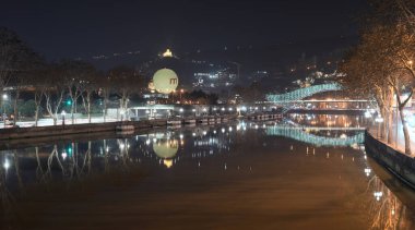 6 Şubat 2026 'da Gürcistan' ın başkenti Tiflis 'teki Kura Mtkvari nehri üzerindeki Barış Köprüsü, çelik ve cam inşaat yaya köprüsü gece görüşü