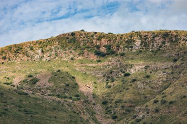 Hindistan, Rajasthan kırsalında, mavi gökyüzü altında kayalık yamaçlar, engebeli dağ manzarası ve dağınık çalılar, doğal doğa ve jeoloji arka planı.