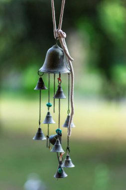 Zincirlenmiş birden fazla küçük çan ile metal rüzgar çanı asılı, halatla dışarıda asılı, yumuşak yeşil bokeh arkaplan, sakin zen ruh hali.