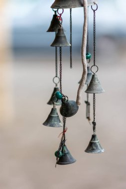 Zincirli, turkuaz boncuklu, sığ alan derinlikli, yumuşak bulanık arka planlı, sakin kırsal dekorlu asılı metal çanların yakın çekimi..