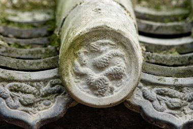 Geleneksel gri seramik kiremitleri yosun ve yuvarlak sırt kapağında oyulmuş ejderha kabartması, sığ alan derinliği, yıpranmış doku.