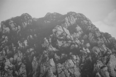 Sisli ve bulutlu gökyüzü, dramatik doku ve doğal doğa manzaralı siyah ve beyaz kayalık dağ uçurumları..